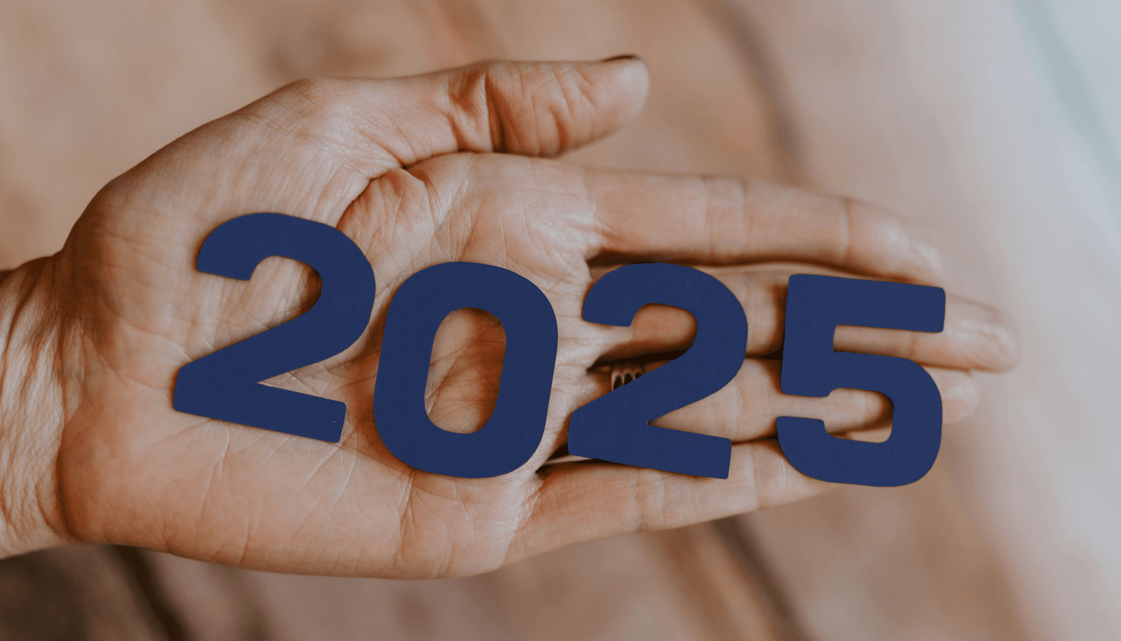 A close-up of a hand holding dark blue numbers forming "2025," symbolising the focus on trends and developments for the year.