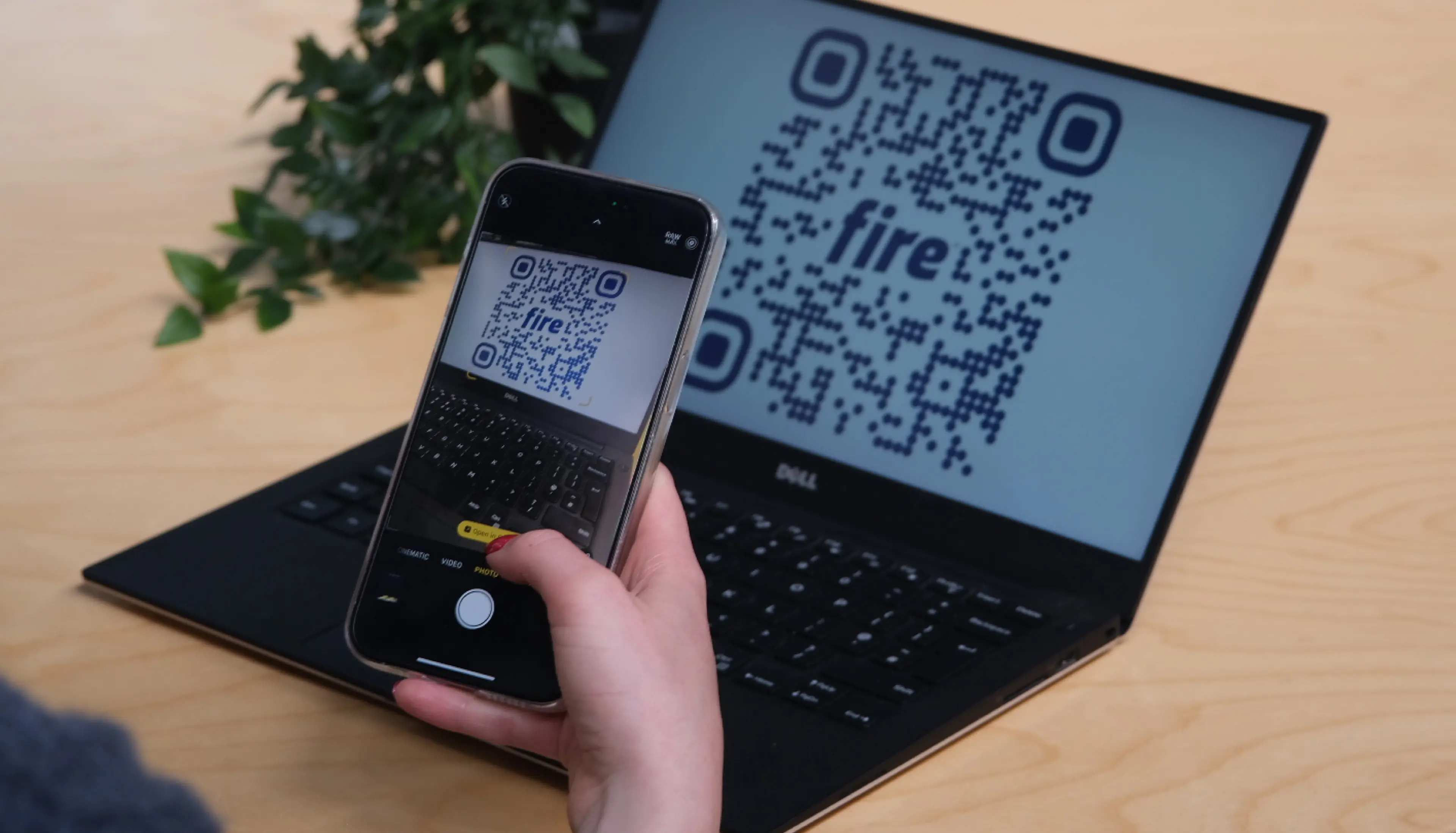 Close-up of a person's hand holding a phone and scanning a Fire payment link QR code displayed on a laptop screen in the background. This demonstrates Fire’s role as an open banking API provider enabling seamless digital payments.