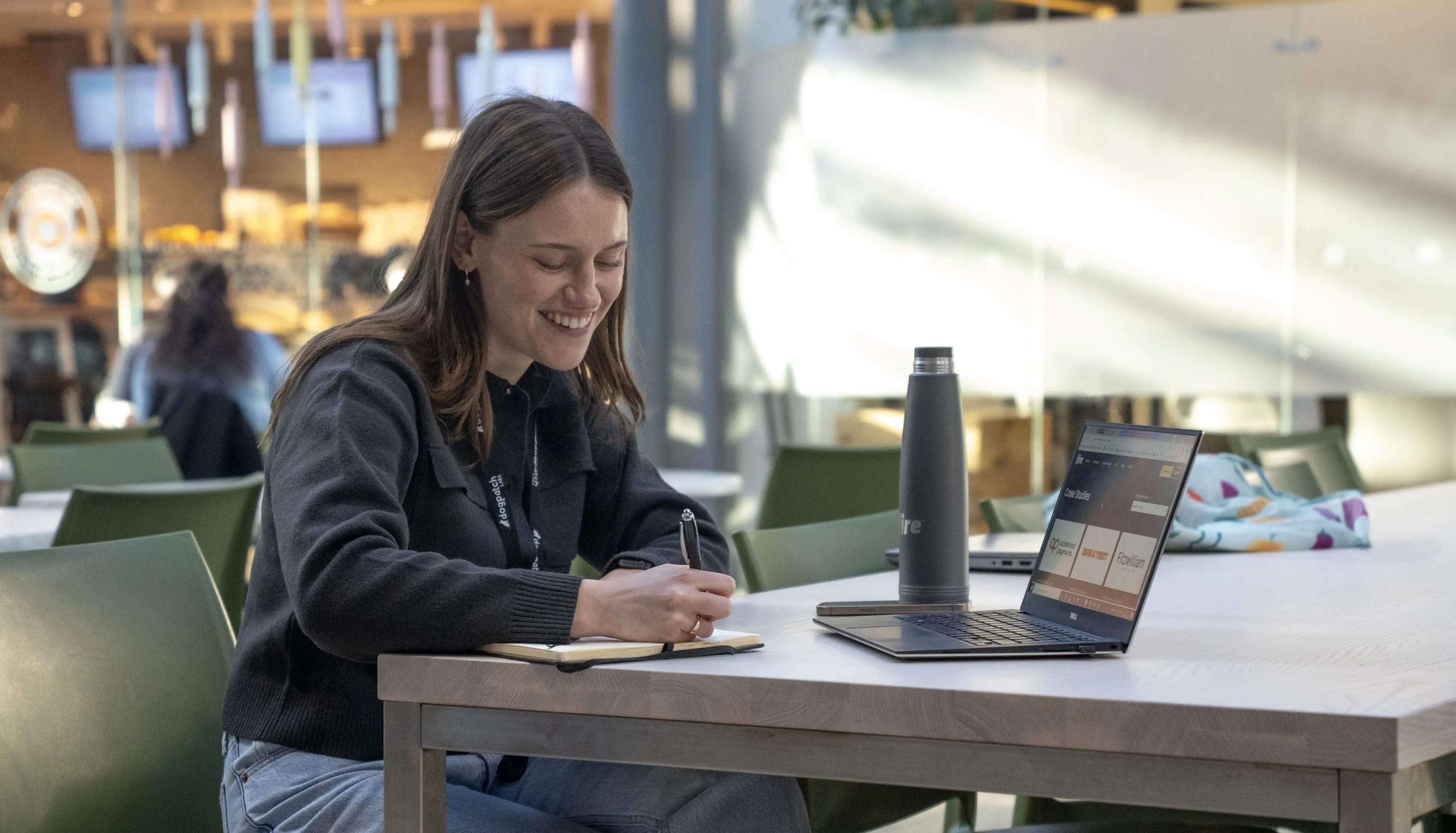 A woman taking notes while viewing the Fire website on her laptop, with a Fire-branded water bottle beside her.