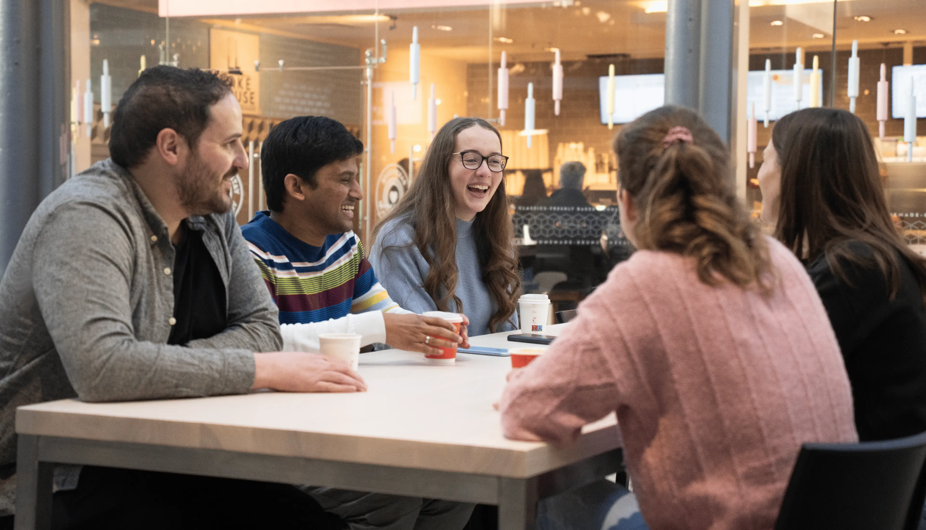 A group of colleagues gathered around a table in a café, engaged in a lively conversation and sharing smiles over coffee.