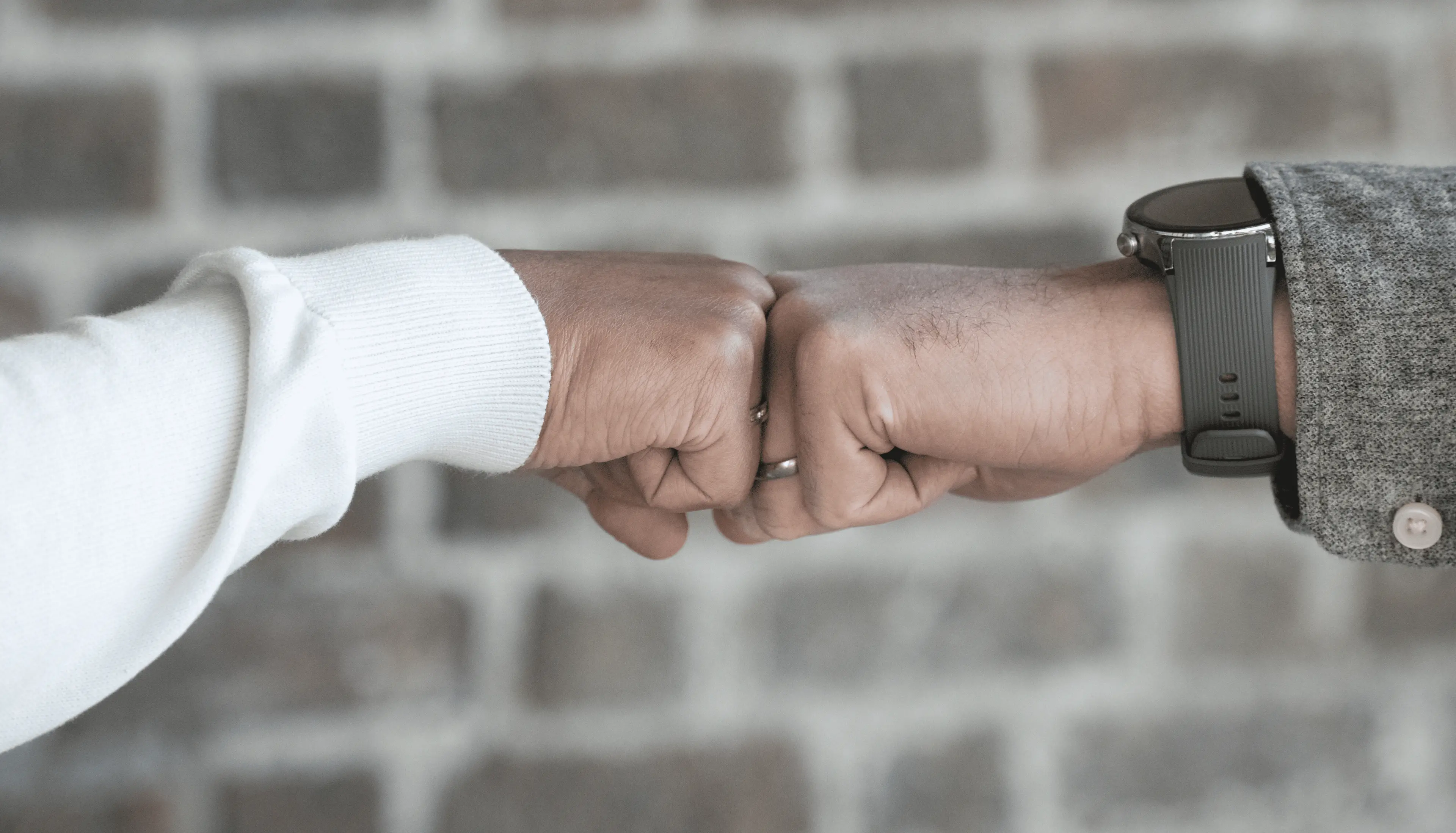 Close-up of two men's hands fist bumping, both wearing wedding bands, with one also wearing a smartwatch.