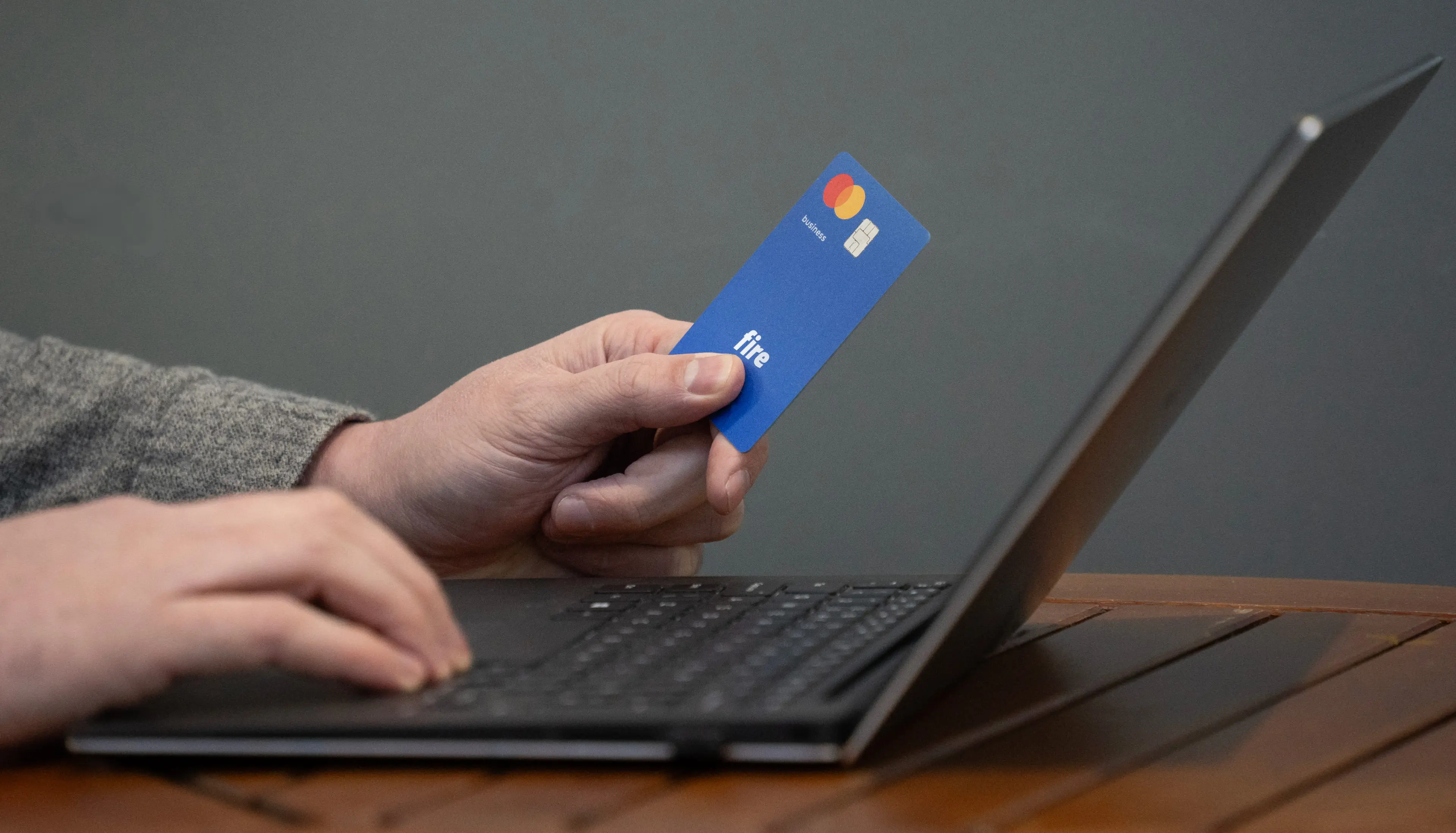 Close-up of a person's hands holding a blue Fire business debit card while using a laptop.