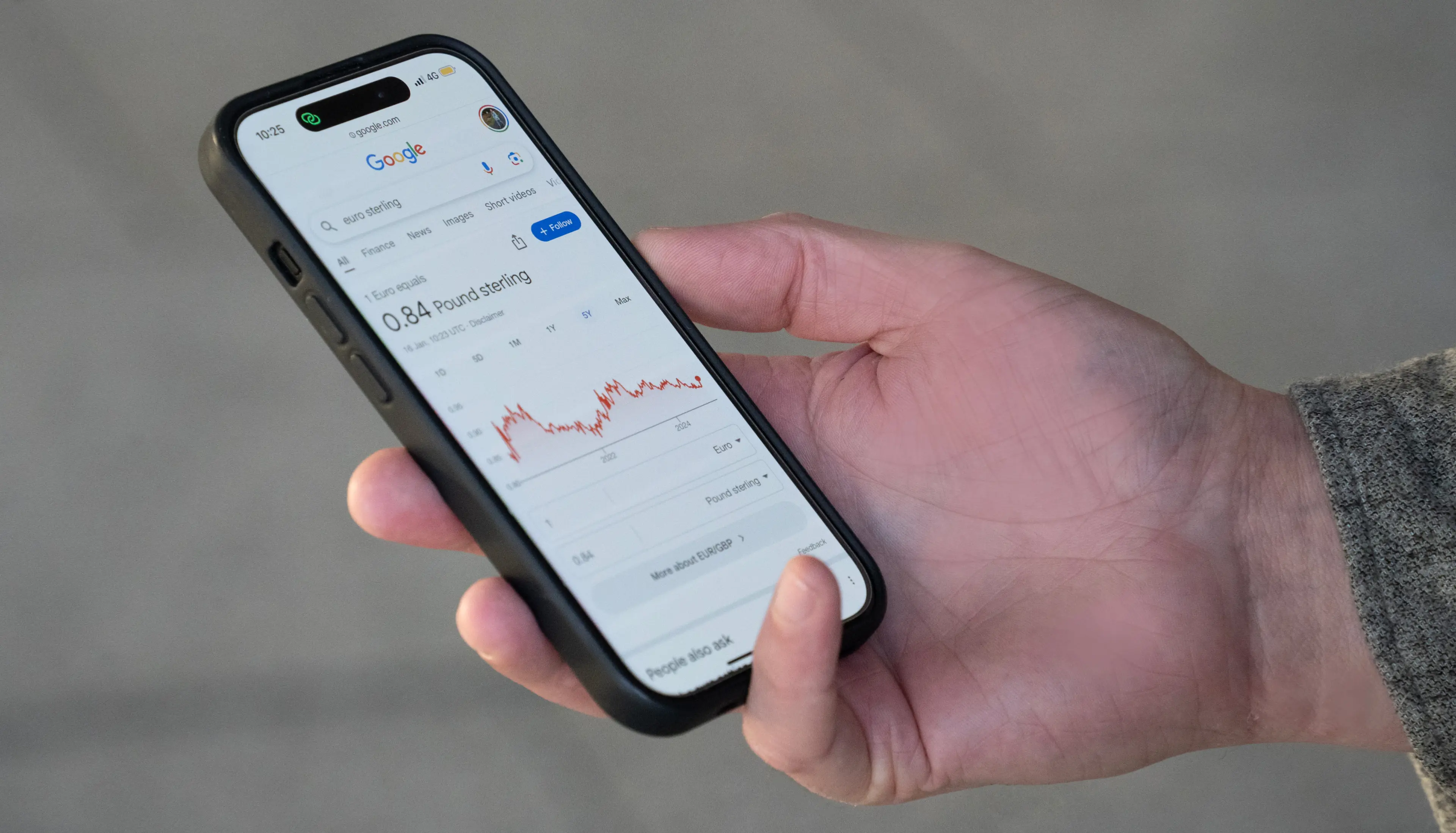 Close-up of a hand holding a phone displaying a euro to sterling exchange rate and a graph of currency fluctuations, representing Fire’s international payments solutions.