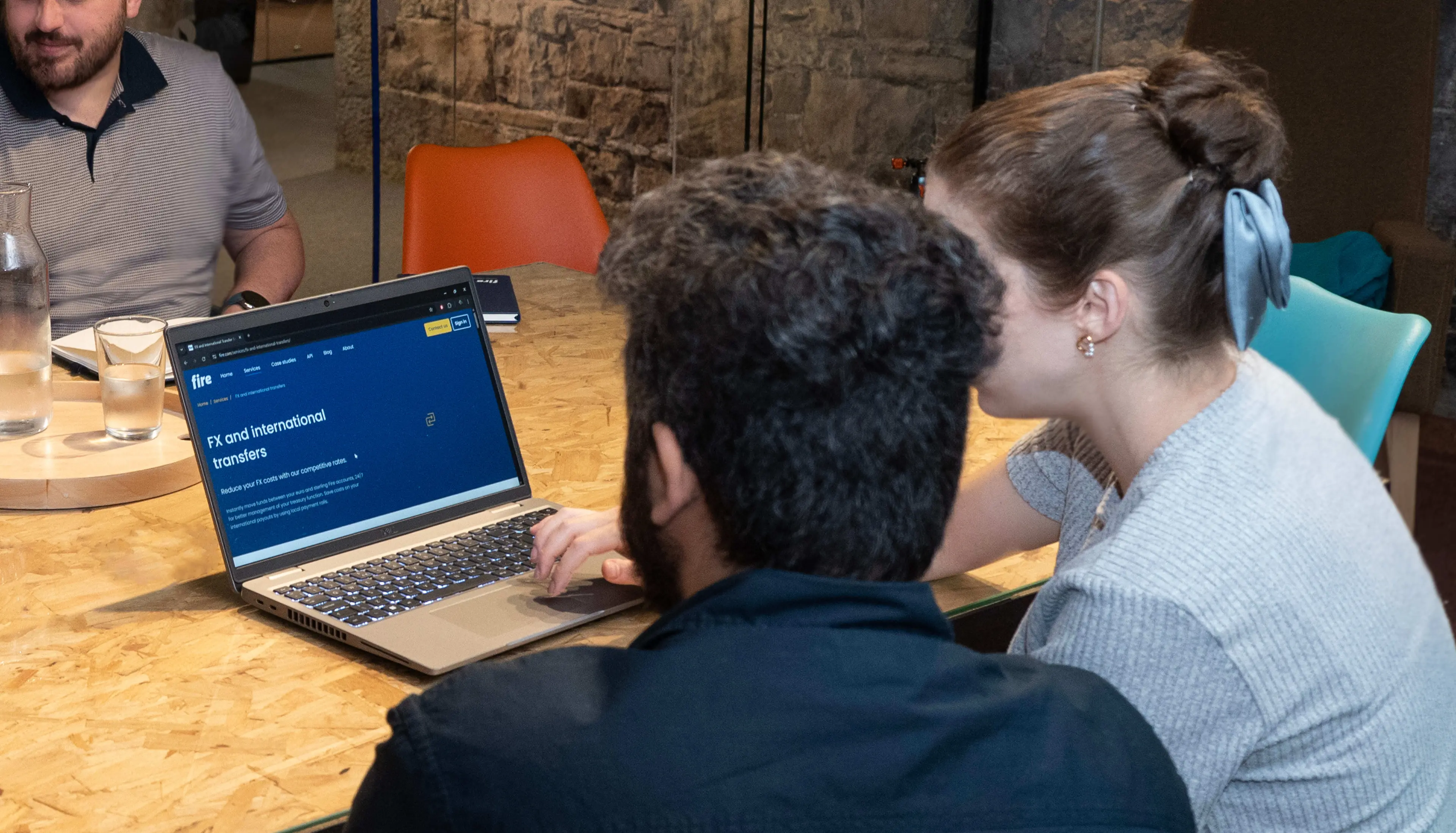 Two people viewed from behind looking at a laptop showing Fire’s FX and international transfers services page, illustrating the use of Fire’s platform for managing cross-border payments.