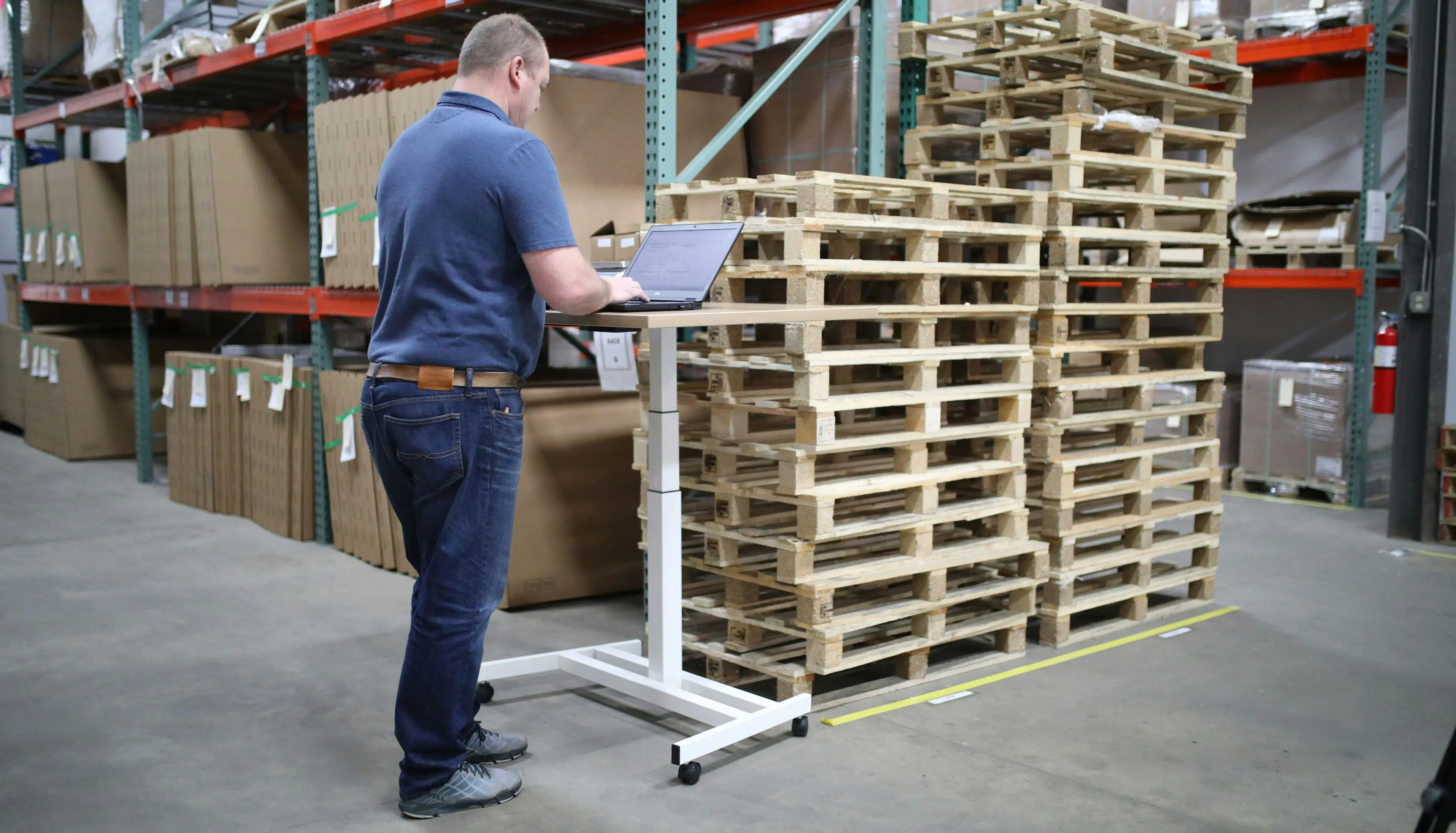 A supply chain manager using modern payment technologies on a laptop in a warehouse, surrounded by pallets and shelves with cardboard boxes.