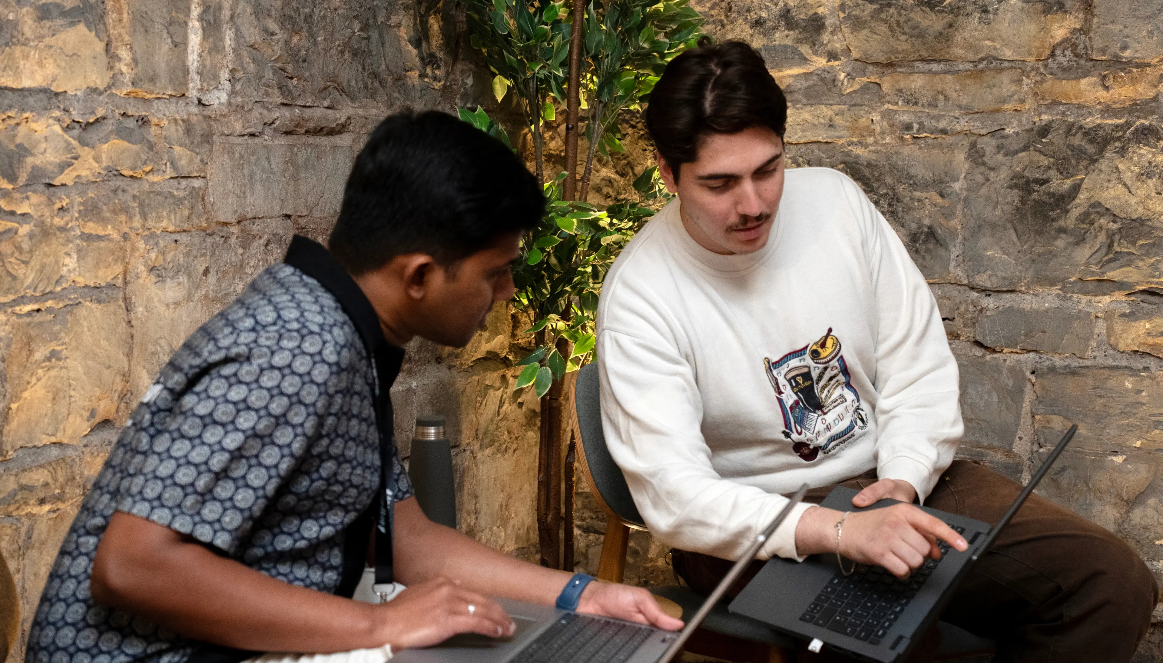 Two men with laptops on their laps, one pointing at the screen while discussing fraud prevention workflows.