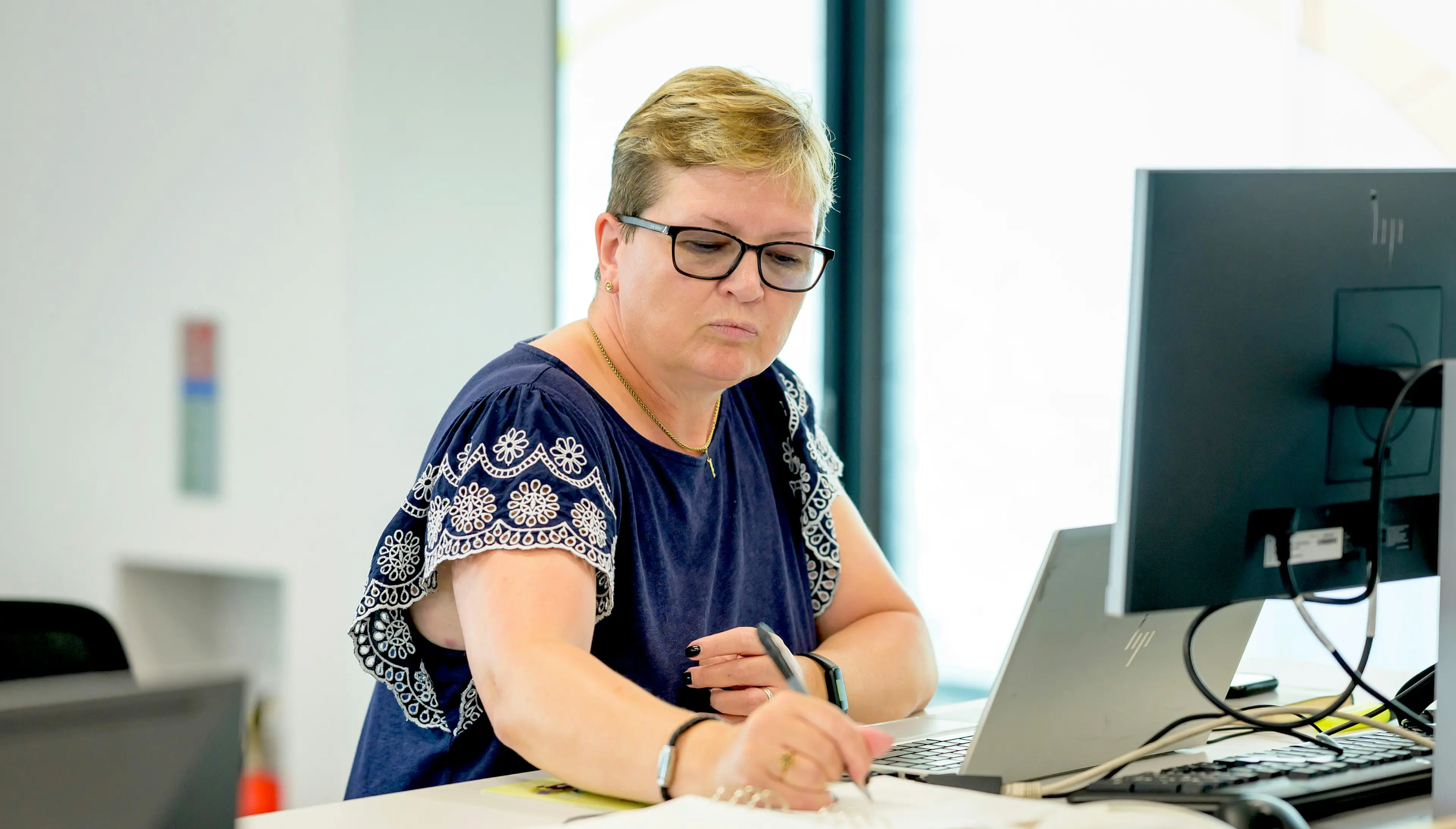 A woman working at a desk with a laptop and computer monitor.