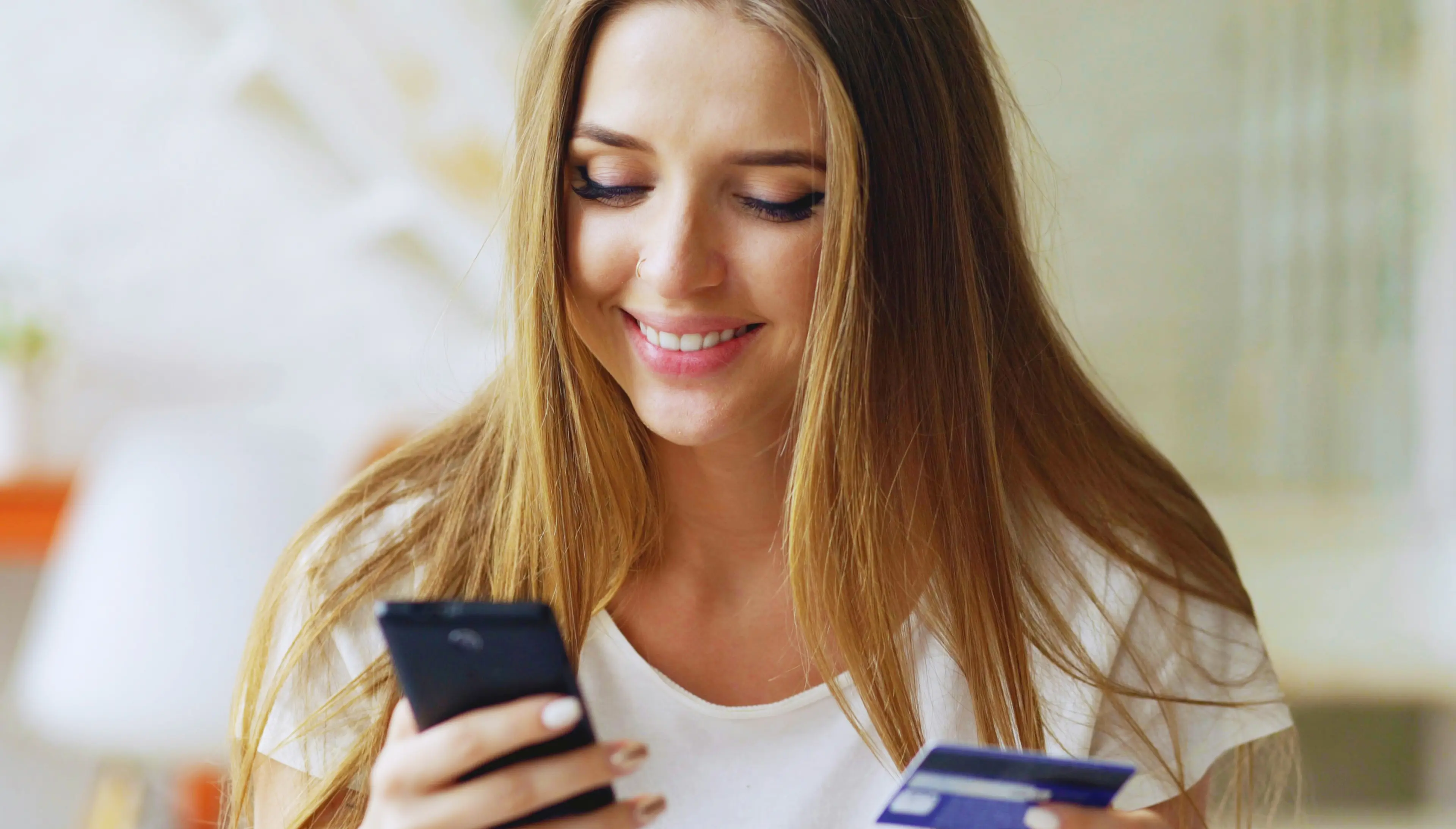 Woman smiling while looking at her phone and holding a bank card.